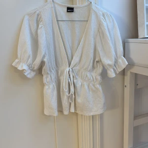 Vit blus från Gina Tricot - Säljer en söt vit blus från Gina Tricot med knytning framtill och puffiga ärnar. Blusen har en v-ringad design och elastisk midja. Den kommer inte till användning men den är i väldigt fint skick! Den köptes här på plick. Skriv om du har fler frågor!