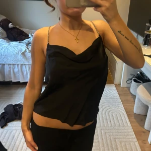 Svart satinlinne med diamant band - Snyggt svart linne i satin med glansigt material och kedjeband som ger en lyxig känsla. Perfekt för en kväll ute. Passar bra till både jeans och kjol😍🙌🏼