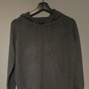 Grå hoodie - Säljer en stilren grå hoodie med långa ärmar och justerbar huva. Perfekt för en avslappnad look. Passar bra till både jeans och mjukisbyxor. 100 merinoull.