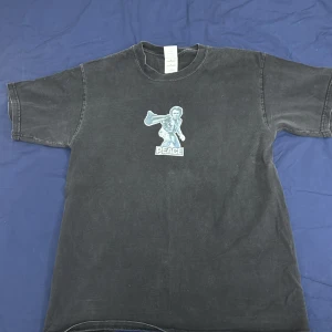 Vintage Svart t-shirt med tryck - Cool svart t-shirt med ett vintageinspirerat tryck av en figur med texten 'PEACE'. T-shirten har en avslappnad passform och korta ärmar, perfekt för en casual look.