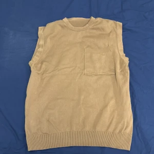 Beige väst från Zara - Säljer en stilren beige väst från Zara. Västen har en enkel design med en bröstficka och ribbade kanter. Perfekt för lager-på-lager-stil.