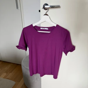 Lila topp från NA-KD - Säljer en söt lila topp från NA-KD med korta ärmar och volangdetaljer vid ärmsluten. Perfekt för en färgglad touch i garderoben! Passar till Xs. Knappt använd, som ny. Kommer från djur & rökfritt hem. 