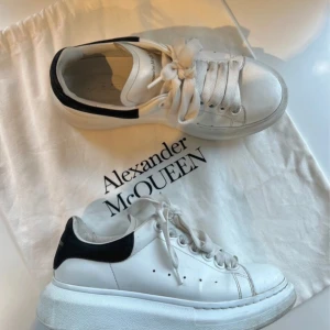 Vita sneakers från Alexander McQueen - Snygga vita sneakers från Alexander McQueen med svart detalj på hälen. Skorna har en chunky sula och klassisk snörning framtill. Perfekta för en stilren look. Storlek 35 ( liten 36) 