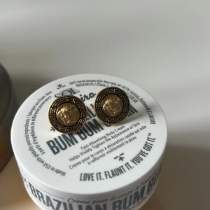 Guldörhängen från Versace - Eleganta guldörhängen från Versace med ett klassiskt mönster och ikonisk design. Perfekta för att ge en lyxig touch till din stil. Dessa örhängen har en rund form och är lätta att bära.