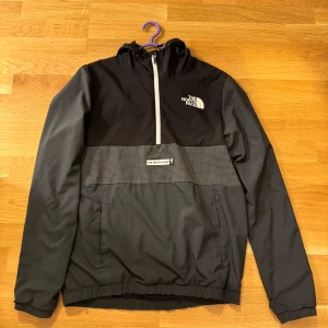 Svart vindjacka från The North Face - Säljer en stilren svart vindjacka från The North Face. Jackan har en halv dragkedja framtill och elastiska muddar vid ärmsluten. Den har även en praktisk ficka på magen med The North Face-logga. Perfekt för blåsiga dagar! Nypris 1199kr