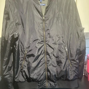 Svart pilotjacka från Gant - Säljer en stilren svart pilotjacka från Gant. Jackan har en dragkedja framtill och två fickor med dragkedjor. Den är långärmad och tillverkad i ett glansigt syntetmaterial. Perfekt för en cool och avslappnad look. Men den är lite sydd under armhålan som ni ser på sista bilden men det är inget man märker av så skriv om ni har funderingar eller liknande 