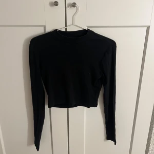 Svart croppad långärmad topp - Säljer en stilren svart croppad topp med långa ärmar. Perfekt för en trendig look. Passar bra till både jeans och kjol. Hör av dig vid intresse!