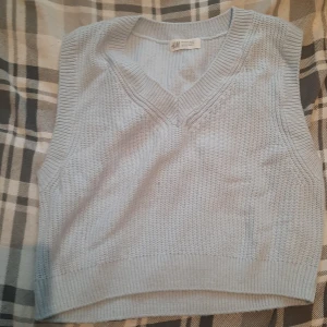 Ljusblå stickad väst från H&M - Säljer en ljusblå stickad väst från H&M med v-ringad design. Perfekt för lager-på-lager och ger en stilren look. Passar bra till både skjorta och t-shirt.