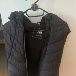 Svart quiltad väst från Zara - Säljer en svart quiltad väst från Zara i storlek S. Västen har en dragkedja framtill och en huva för extra värme. Perfekt för lager-på-lager under kyligare dagar.