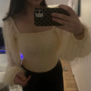 Gul offshoulder topp - Säljer en elegant gul offshoulder topp med långa, fluffiga ärmar. Toppen har en smockad design som ger en tight passform och en mjuk, luftig känsla. Perfekt för en stilren look.