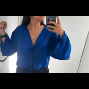 Blå blus med knytning S heltny - Säljer en snygg blå blus med knytning framtill. Blusen har en v-ringad design och vida ärmar som ger en avslappnad look. Perfekt för att piffa upp garderoben!