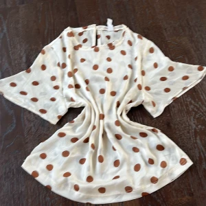 Vit prickig blus från Mango - Säljer en söt vit blus från Mango med bruna prickar. Blusen har korta ärmar  och en knappdetalj i nacken. Perfekt för sommaren, vardag eller finare tillfällen. Blusen är helt oanvänd och är därför i super fint skick. Hör gärna av er vid frågor och funderingar💛