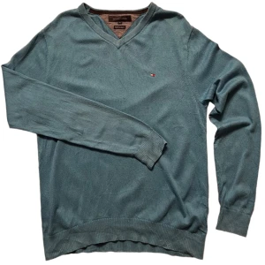 Blå tröja från Tommy Hilfiger - Snygg blå tröja från Tommy Hilfiger i bomull och kashmir. Tröjan har en v-ringad hals och ett litet broderat märke på bröstet. Perfekt för en stilren look.