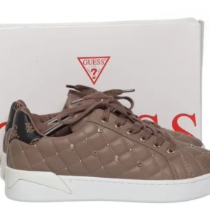 Bruna quiltade sneakers från Guess - Snygga bruna sneakers från Guess med quiltad design och snörning. Skorna har en vit sula och detaljer i svart med mönster på hälen. Perfekta för en stilren look.