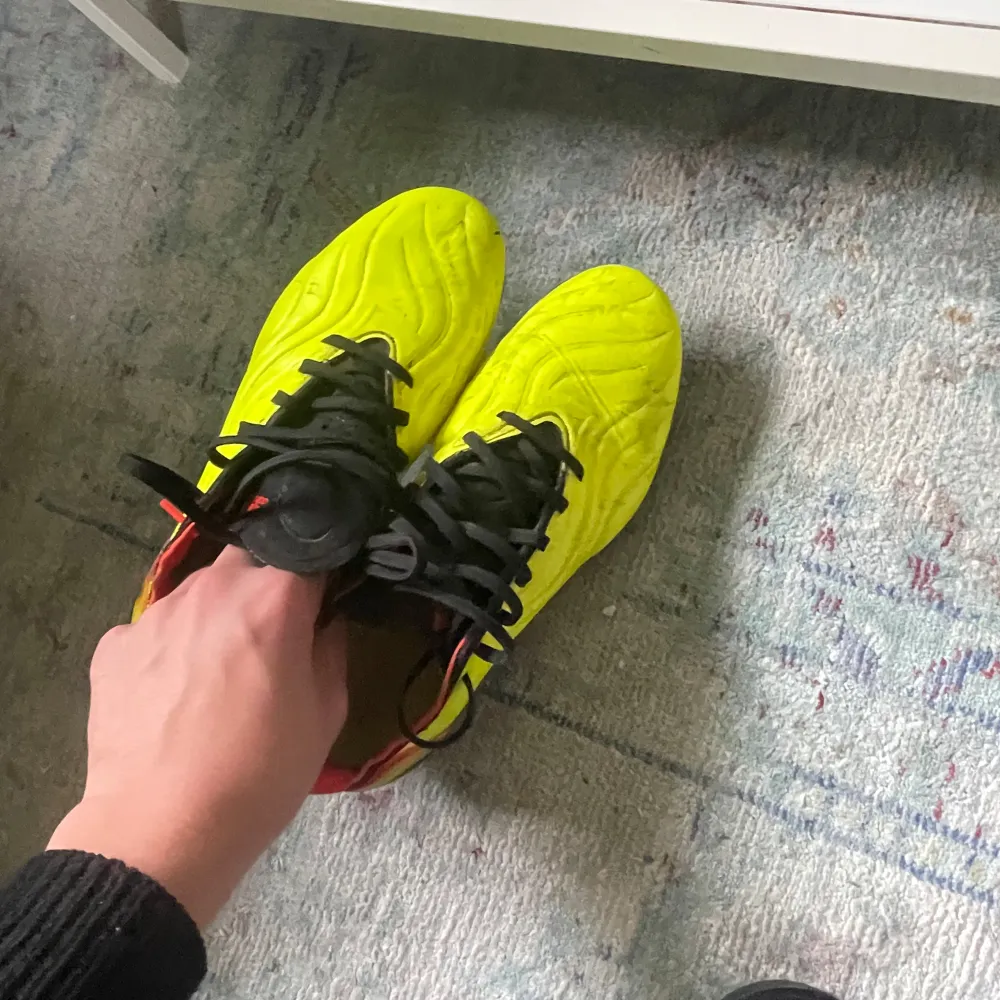 Snygga gula fotbollsskor från Adidas med svarta och röda detaljer. Perfekta för fotbollsspelare som vill sticka ut.. Kengät.