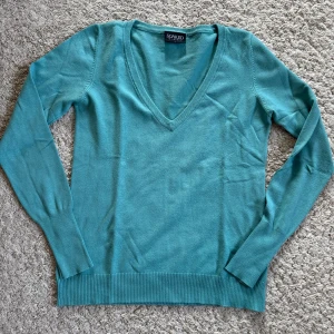 Turkos tröja från Soaked in Luxury - Säljer en stilren turkos tröja från Soaked in Luxury. Tröjan har en v-ringad design och är tillverkad i en mjuk blandning av viskos och elastan. Perfekt för en avslappnad och chic look.