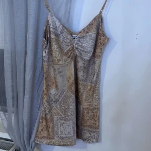 Mönstrad linne från Stradivarius - Säljer en snygg linne från Stradivarius med ett unikt paisleymönster i beige och bruna toner. Linnet har smala axelband och en v-ringad design som ger en elegant look. Perfekt för varma dagar eller en stilfull kväll. 🌟