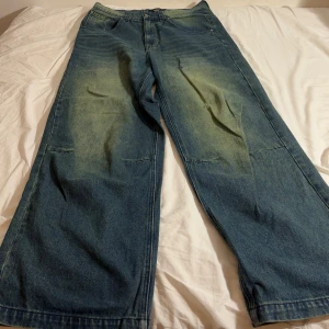Blå-Gröna Jeans från Jaded London - Säljer ett par grönblåa colossus jeansbyxor från Jaded London med en baggy passform. Byxorna har en cool, sliten look med ljusare partier på framsidan och baksidan. Perfekta för en avslappnad stil. Notera viss defekt på botten av jeansen. Nypris är 1 350 kr. 