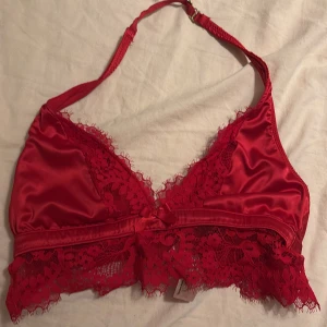 Röd spetsdetaljerad topp från Hunkemöller - Snygg röd topp från Hunkemöller med spetsdetaljer och justerbara axelband. Perfekt för en elegant look med en feminin touch. Toppen har en v-ringad design och en dekorativ rosett framtill.