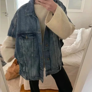 Blå jeansjacka - Säljer en klassisk blå jeansjacka med knappar framtill och två bröstfickor. Jackan har en avslappnad passform och är perfekt för lager-på-lager-stil. Den har en tidlös design som funkar till många olika outfits. En knapp saknas på ena sidan dock.