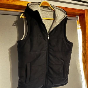 Svart och grå vändbar väst med huva - Otroligt fet väst som man kan vända ut och in. Alltså får du en svart och en grå väst. De svarta är mocka medan de grå är typ mjukt tyg. Storlek m men passar även större. Ny skick.