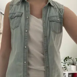 Säljer en snygg ljusblå jeansväst från H&M. Västen har knappar framtill och två bröstfickor med lock. Perfekt för att ge din outfit en cool touch. Passar bra till både t-shirt och långärmad tröja. Västen är i storlek 146 men jag skulle säga åt den passar en 158/164!