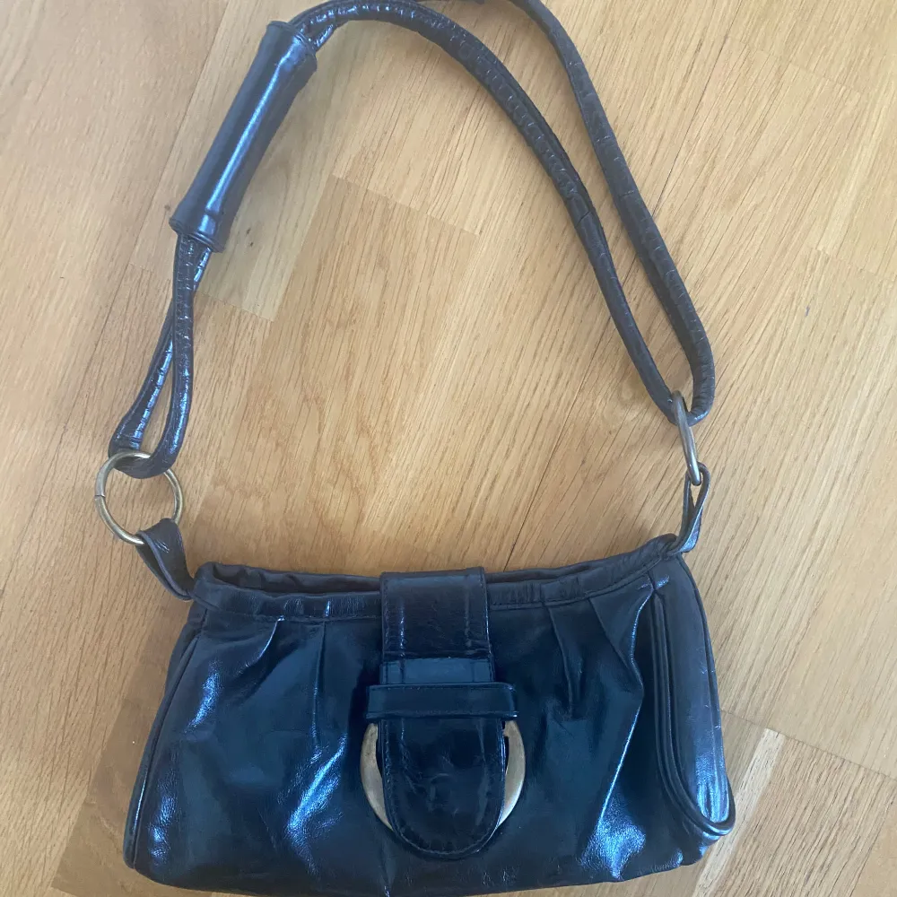 Svart axelväska från Venezia i skinn. Väskan har en justerbar axelrem och en dekorativ metallspänne framtill. Perfekt för att bära dina nödvändigheter med stil. Genuine leather made in Italy. . Laukut & Käsilaukut.