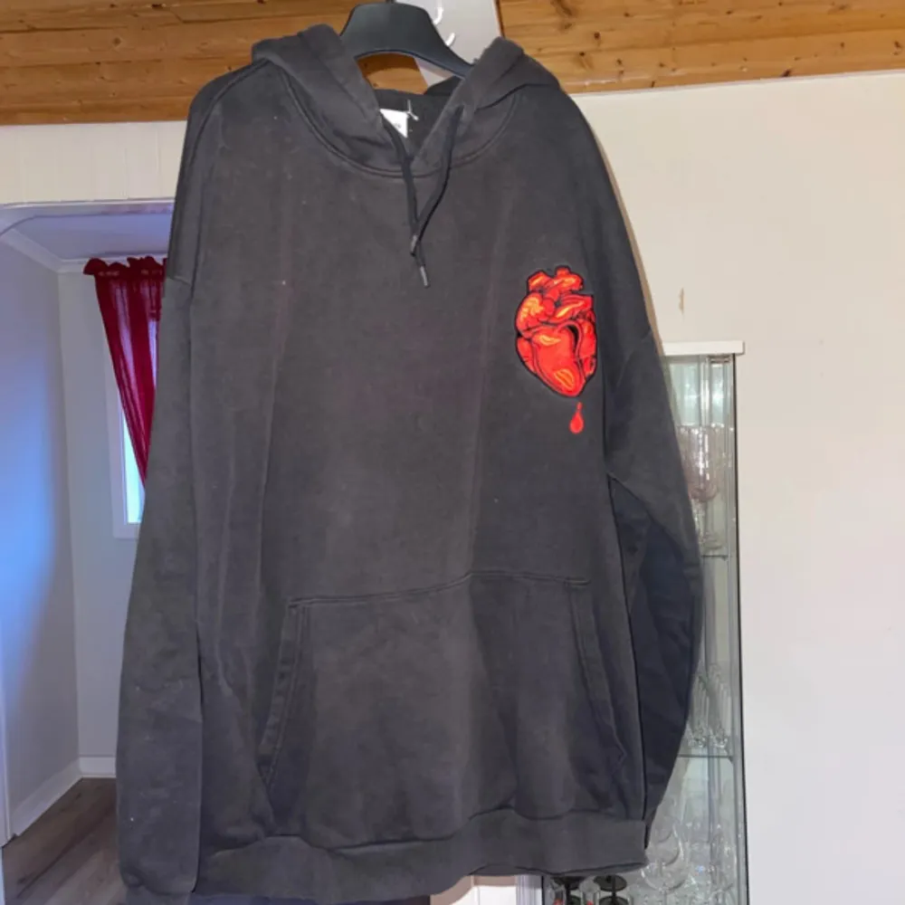 Säljer en svart hoodie med ett rött hjärta tryckt på framsidan och ett stort tryck på baksidan med texten 'Broken Heart Club'. Hoodien har en klassisk passform med känguruficka och justerbar huva.. Neuletakit & Villapaidat.