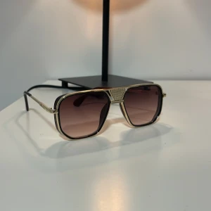 Solglasögon från Maybach - Snygga solglasögon från Maybach med en lyxig känsla. De har en fyrkantig form med guldiga detaljer och mörka linser som ger ett elegant intryck. Perfekta för att höja din stil till nästa nivå.