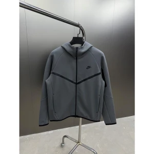 Nike tech grå - Säljer en stilren grå hoodie från Nike med dragkedja och huva. Jackan har en modern design med svarta detaljer och Nike-logga på bröstet. Perfekt för en sportig look. Finns alla storlekar S M L XL XXL