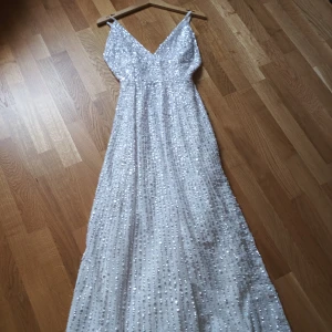 Vit glittrig långklänning från ASOS - Säljer en fantastisk vit långklänning från ASOS med glittrande paljetter över hela tyget. Klänningen har en v-ringad design och smala axelband, perfekt för en elegant kväll.