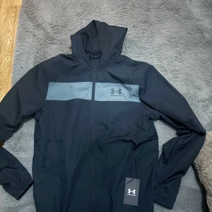 Svart vindjacka från Under Armour - Säljer en jacka från Under Armour som är helt oanvänd med prislapp på. 