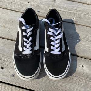 Säljer ett par klassiska Vans sneakers i svart och vitt. Skorna har en snygg design med vit sula och vita snören. De är i storlek dam 36 och har den ikoniska 'Off the Wall' loggan på hälen. Perfekta för vardagsbruk och ger en skön streetstyle-look. De är i nyskick!