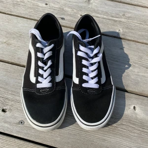 Svarta och vita sneakers från Vans - Säljer ett par klassiska Vans sneakers i svart och vitt. Skorna har en snygg design med vit sula och vita snören. De är i storlek dam 36 och har den ikoniska 'Off the Wall' loggan på hälen. Perfekta för vardagsbruk och ger en skön streetstyle-look. De är i nyskick!