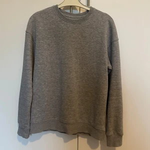 Grå sweatshirt från Jack & Jones - Säljer en stilren och bekväm grå sweatshirt från Jack & Jones. Perfekt för både vardag och mysiga hemmakvällar. Tröjan har långa ärmar och en klassisk rund halsringning. Passar till det mesta i garderoben!