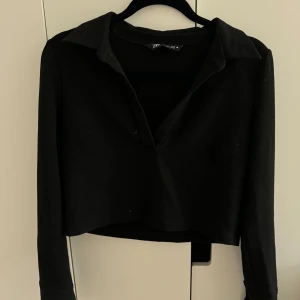 Svart croppad tröja från Zara - Säljer en svart croppad tröja från Zara. Den har långa ärmar och en klassisk krage. Snygg nere vid handlederna, ”slits” och knappar 