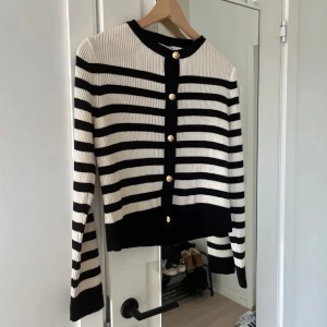 Randig kofta med guldknappar - Säljer en superfin randig kofta i svart och vit med snygga guldknappar framtill. Den är ribbad och har långa ärmar, perfekt för både vardag och fest. Koftan är i nyskick och passar perfekt till höst 🎀