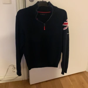 Mörkblå tröja från Henri Lloyd - Säljer en mörkblå tröja från Henri Lloyd med en halv dragkedja och en Union Jack-detalj på ärmen. Tröjan har långa ärmar och ribbade muddar. Perfekt för kyligare dagar. Tröjan är i nyskick   Köpt för Cirka 1000kr Säljer nu för endast 320!