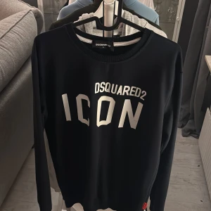 Svart långärmad tröja från Dsquared2 - Snygg svart långärmad tröja från Dsquared2 med texten 'ICON' i vitt på framsidan. Perfekt för en stilren och modern look. Tröjan har en rund halsringning och är tillverkad i ett mjukt material. Storlek L men den är väldigt liten för att vara en sån stor storlek