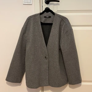 Grå kavaj från Bikbok - Snygg grå kavaj från Bikbok med en enkel knapp framtill. Den har en stilren design med långa ärmar och en v-ringad öppning. Perfekt för en chic och minimalistisk look.