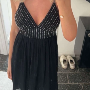 Svart klänning med paljetter Zara - Snygg svart klänning med v-ringad urringning och glittriga paljettdetaljer på överdelen. Perfekt för en festlig kväll. Klänningen har en luftig kjol som ger en elegant look. 