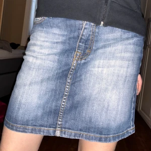 Jeanskjol från L.O.G.G. - Snygg jeanskjol från L.O.G.G. i klassisk blå denim. Kjolen har en kort längd och en stilren design med synliga sömmar och fickor fram. Perfekt för en sommardag eller bara för vardagen.