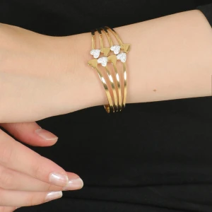 Guldarmband med hjärtan  - Elegant guldarmband med flera hjärtformade detaljer prydda med glittrande strass. Perfekt för att ge en lyxig touch till din outfit. Armbandet har en öppen design som gör det enkelt att justera. .14k Guldpläterad.