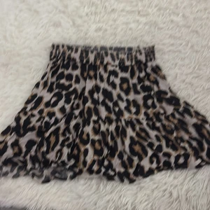 Leopardmönstrad kjol - Snygg leopardmönstrad kortkjol med volanger. Perfekt för att ge en vild touch till din outfit. Den har en elastisk midja för bekväm passform. 🐆