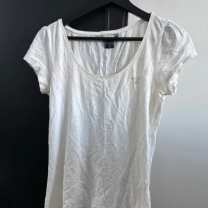 Vit kortärmad topp från GANT - Säljer en stilren vit topp från GANT med korta ärmar och rund halsringning. Perfekt för en enkel och klassisk look. Passar bra till både jeans och kjol.