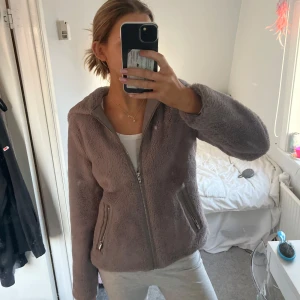 Grå pälsjacka med dragkedja - Mysig grå pälsjacka med dragkedja framtill och två fickor med dragkedjor. Jackan har en luva och är långärmad. Kommer inte till användning då den är lite för liten för mig!❤️‍🔥