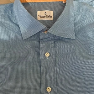 Blå skjorta från Emanuel Berg - Snygg blå skjorta från Emanuel Berg med ett diskret rutmönster. Skjortan har klassisk krage och knappar framtill. Perfekt för en stilren look.