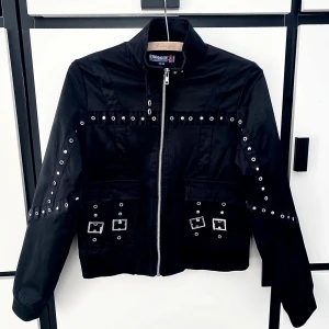 Brooker jacka - Snygg svart jacka från Brooker med coola nitar och dragkedja framtill. Jackan har långa ärmar och flera fickor med spännen. Perfekt för en edgy look!