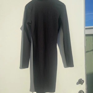 Svart ribbad klänning från Boohoo - Snygg svart ribbad klänning från Boohoo med lång ärm och v-ringad hals. Perfekt för en stilren look. Klänningen har en tight passform som framhäver figuren.använd 1 gång. Helt ny 