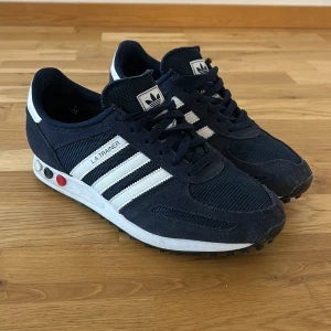 Adidas LA Trainer  - Snygga Adidas LA Trainer sneakers i marinblått med vita detaljer och klassiska tre ränder. Skorna är i bra skick och passar perfekt nu inför våren!